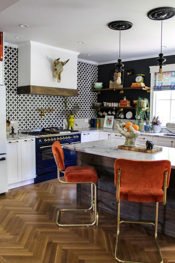 a bold eclectic kitchen with white cabinets, a navy cooker, a kitchen island, rust-colored stools and a hood over the cooker