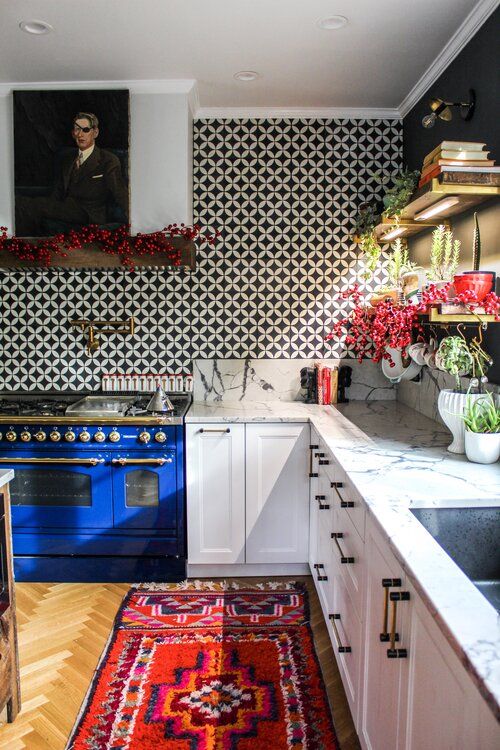 a bold eclectic kitchen with white shaker style cabinets, a bold blue cooker, a bright rug, a black and white tile backsplash and a portrait