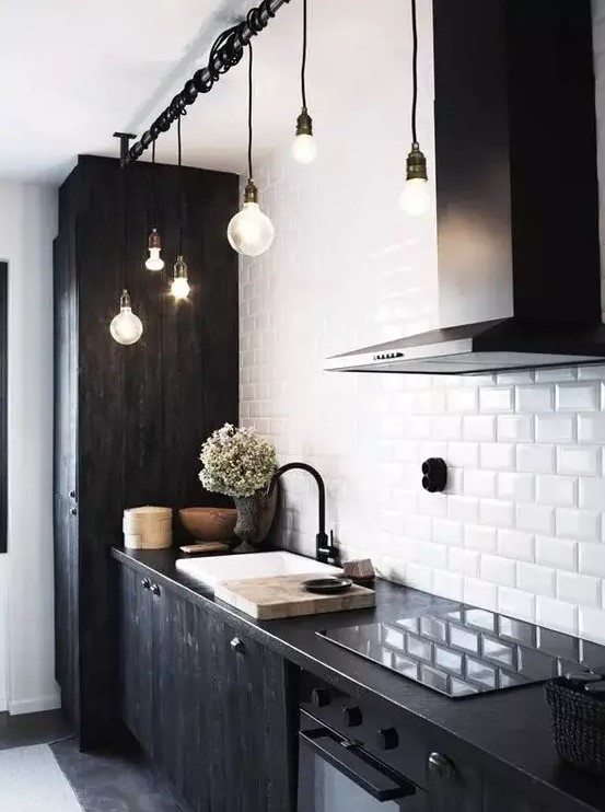 a bold kitchen with black wood cabinets, a white subway tile kitchen backsplash, black countertops and black pendant bulbs