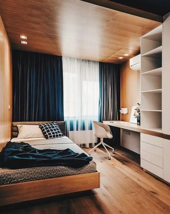 a bold minimalist teen room with a wooden ceiling with lights, navy curtains, a storage unit with a built in desk, a comfy bed and blue bedding