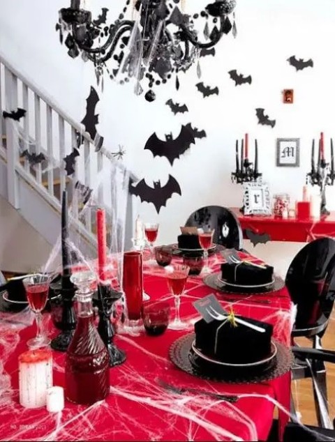 a bold red and black Hallloween tablescape with spiderwebs, red vases and goblets, black plates and boxes, bats and a black chandelier
