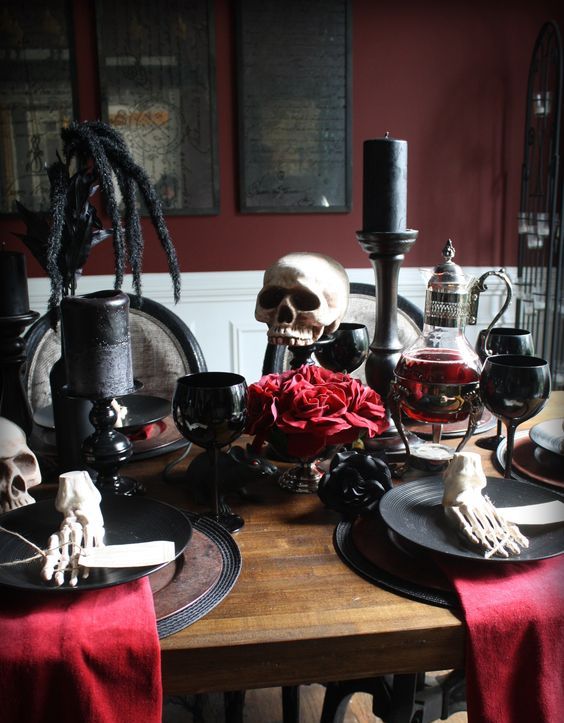 a bold red and black Halloween tablescape with black placemats and plates, black candles and glasses, red napkins and red blooms