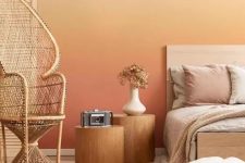 a bold warm-colored bedroom with a gradient wall from neutral to rust, a bed with neutral bedding, tree stump nightstands, a papasan chair