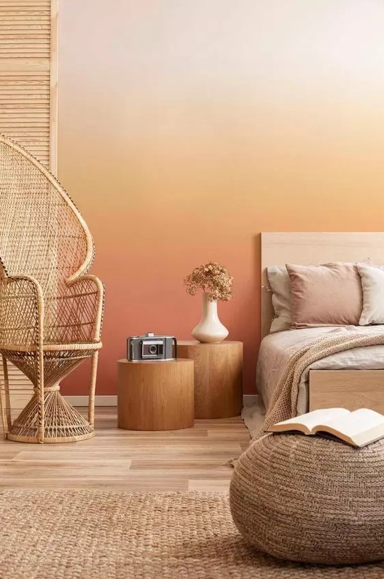 a bold warm colored bedroom with a gradient wall from neutral to rust, a bed with neutral bedding, tree stump nightstands, a papasan chair