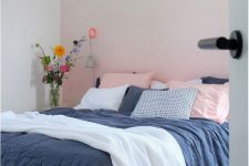 a bright bedroom with an ombre pink accent wall, a bed with navy and white bedding and some bright blooms