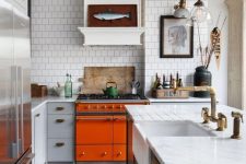 a bright eclectic kitchen with an orange cooker, navy and grey cabinets, white stone countertops and catchy artworks