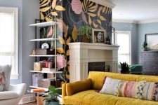 a bright eclectic living space with a unique chandelier, a mustard velvet sofa, a boho rug, a floral fireplace wall
