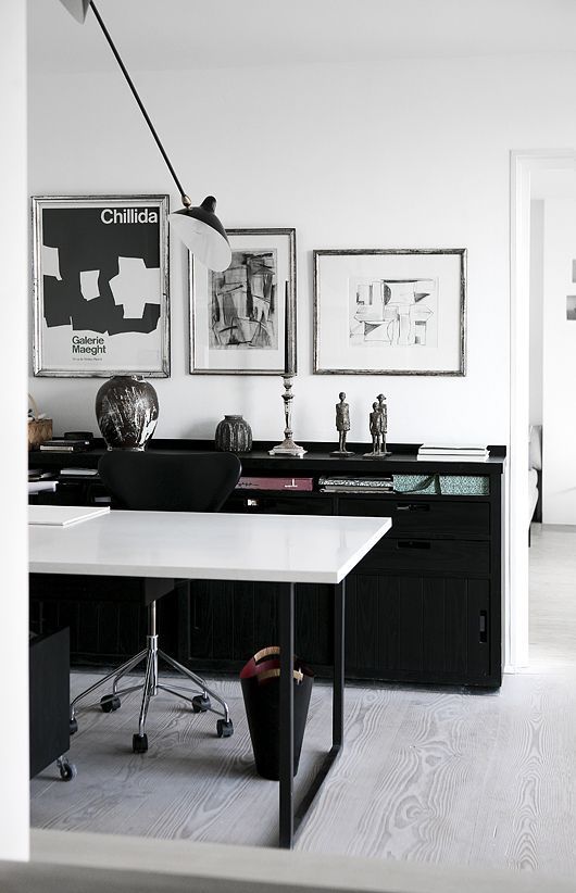 a catchy and stylish black and white home office with a black storage unit, a black and white desk, a black chair and a mini gallery wall of three pieces