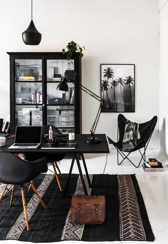a catchy boho black and white home office with a black storage unit, a black desk and chairs, black lamps and a boho printed rug plus greenery