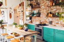 a catchy eclectic kitchen with emerald cabinets, white countertops, a stainless steel cooker, a table on casters and stool plus lots of plants