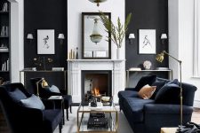 a chic black and white interior with a working fireplace, a couple matching consoles, a black vintage sofa and chairs, a large crystal chandelier