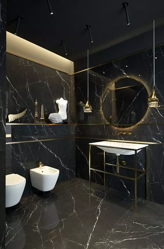 a chic contemporary black and gold bathroom with a lit up round mirror, white appliances, pendant lamps and black marble tiles all over