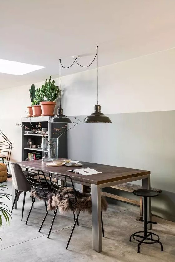 a chic industrial dining space with a grey storage unit, a wood and metal table, black metal chairs and stools and black pendant lamps