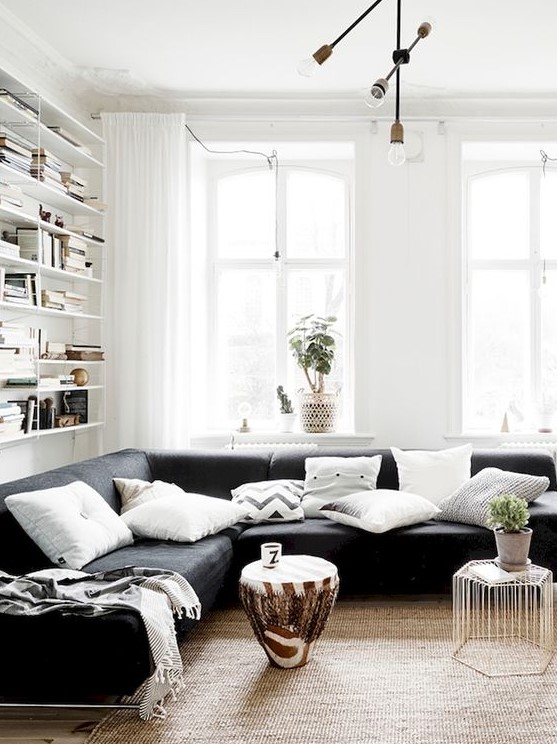 a chic living room with shelves, a black sectional, a couple of catchy coffee tables and a jute rug