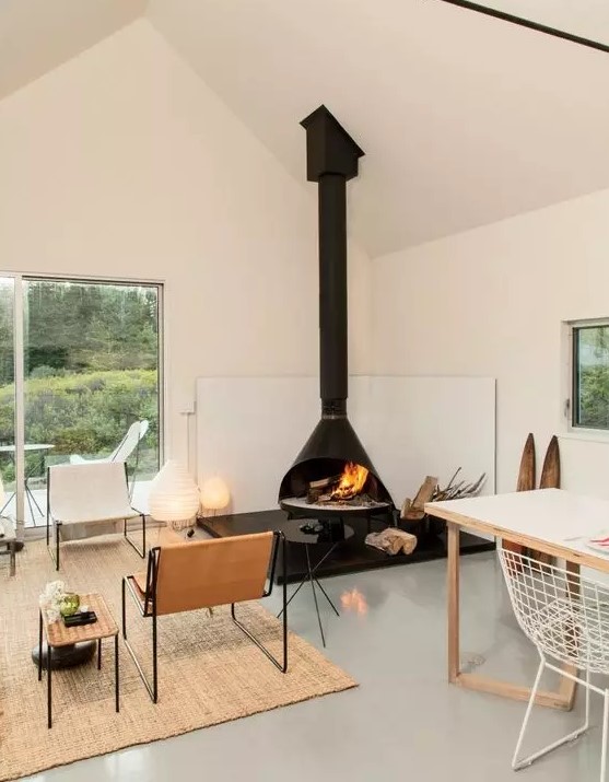 a chic modern living and dining space wiht a black Malm fireplace, leather chairs, a woven coffee table, a white dining table and white metal chairs