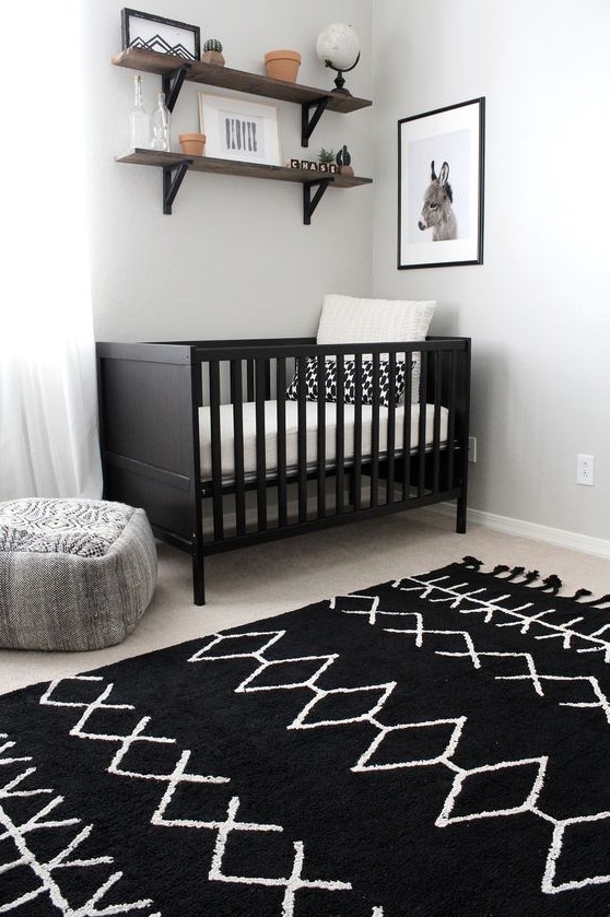 a chic nursery with a black crib, a printed rug, wooden shelves and a pretty artwork for a simple andd cozy space