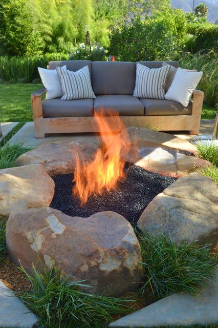 a chic outdoor space with a grey sofa and a fire pit clad with large rocks and with grass is a lovely idea for any garden