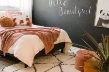 a chic teen bedroom with a chalkboard wall, a bed with pretty pink bedding, a wooden desk, a chair and a footrest