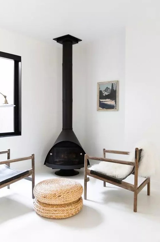 a clean and chic sitting nook with a black Malm fireplace, black leather chairs, jute poufs and all white everything around