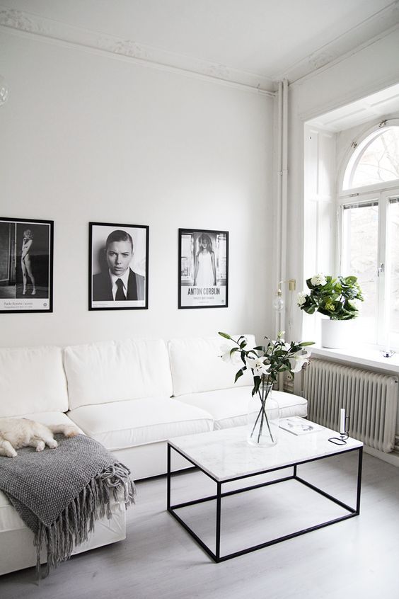 a clean white Scandinavian living room with a sectional, a coffee table, greenery and just a bit of black touches