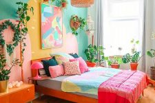 a colorful eclectic bedroom with an emerald accent wall, a red bed with colorful bedding, a bright artwork, potted plants, an orange credenza