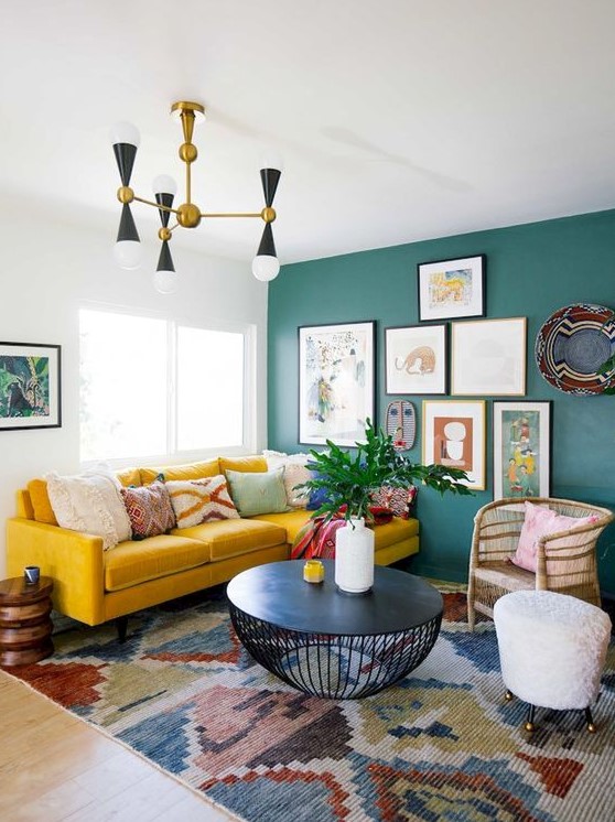 a colorful eclectic living room with a green statement wall with artworks, a boho rug, a mustard sofa and wicker touches