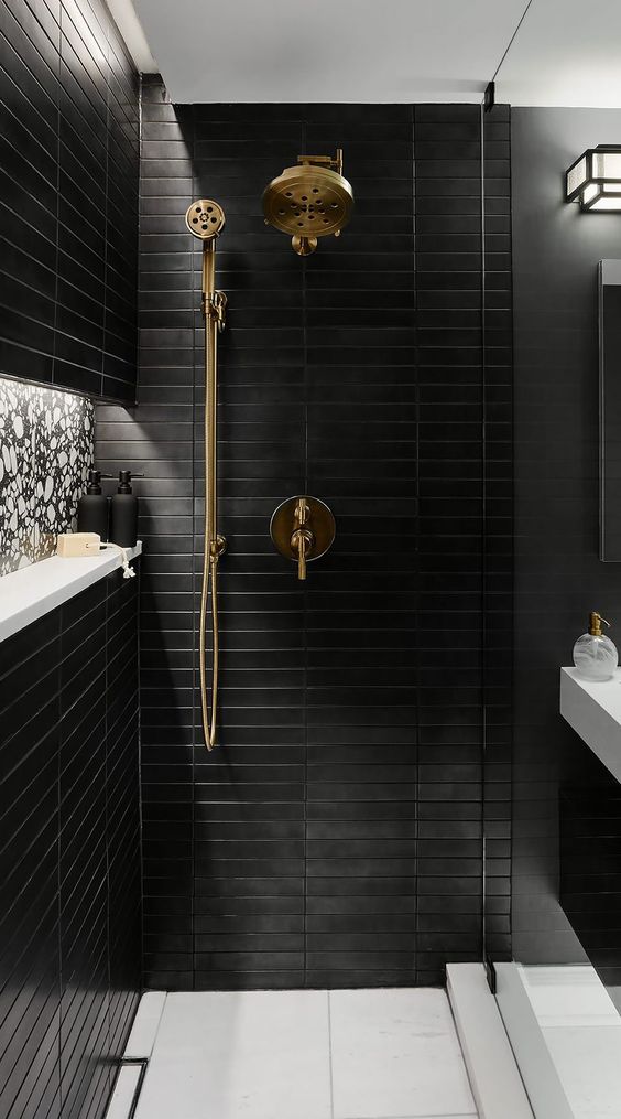 a contemporary bathroom clad with large scale neutral and skinny black tiles, a niche and a wall-mounted sink, gold fixtures