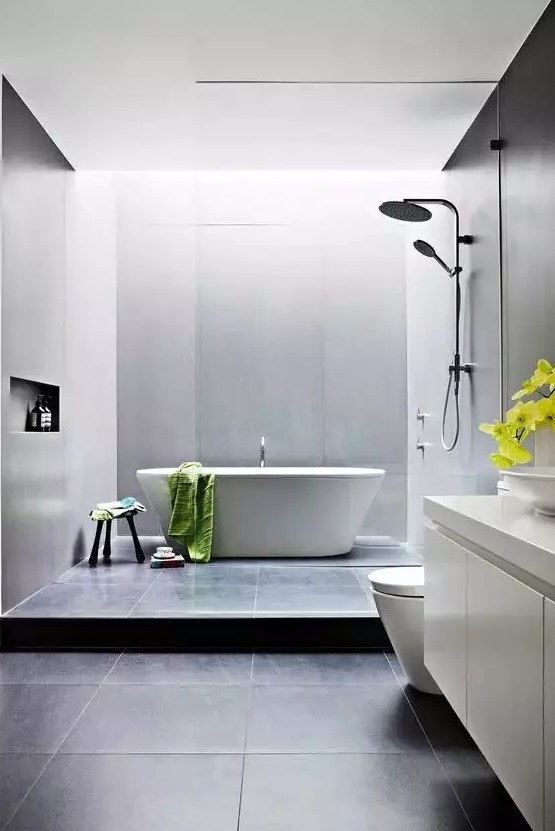 a contemporary bathroom with black and grey large scale tiles, a tub, a floating white vanity, white appliances and neutral fixtures