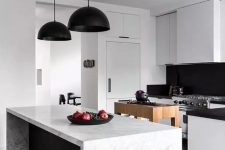 a contemporary black and white kitchen with sleek cabinets, black countertops and a backsplash, black pendant lamps