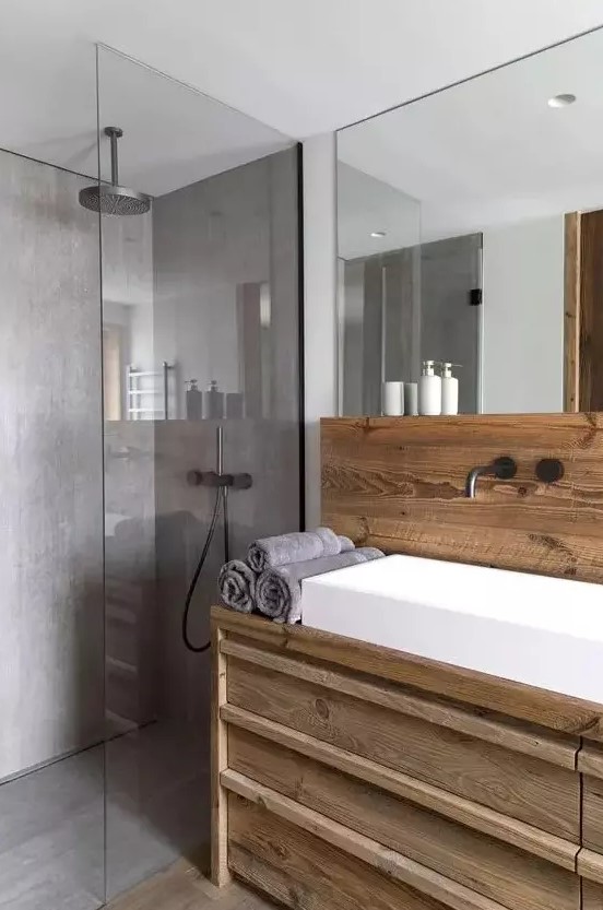 a contemporary chalet bathroom clad with wood and with lots of concrete in decor, with a large mirror, a white sink and a rainshower