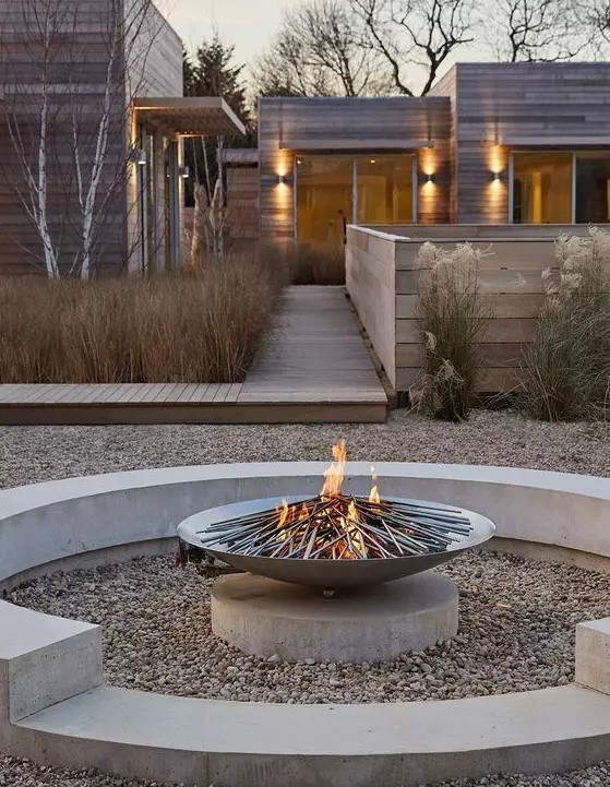 a contemporary fire pit of concrete, with pebbles on the ground and a metal fire bowl looks chic and very edgy
