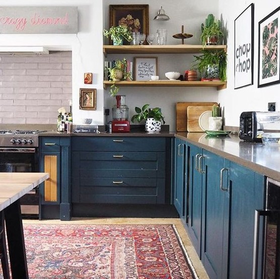 a contemporary meets boho kitchen with a boho rug, navy cabinets, a stone countertop and potted plants