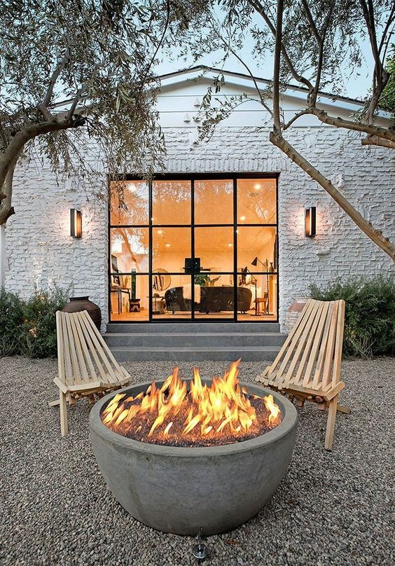 a contemporary outdoor space done with gravel, a couple of wooden chairs and a concrete fire bowl is amazing