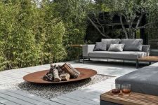 a contemporary outdoor space with grey sofas and wooden side tables, a greyish deck and a fire bowl in its center