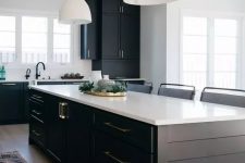 a contrasting kitchen with black planked cabinets and a kitchen island, white countertops and white pendant lamps