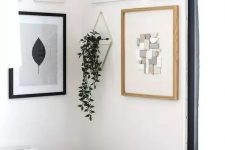 a cool modern gallery wall with mismatching white, black and neutral frames and various types of art plus hanging greenery