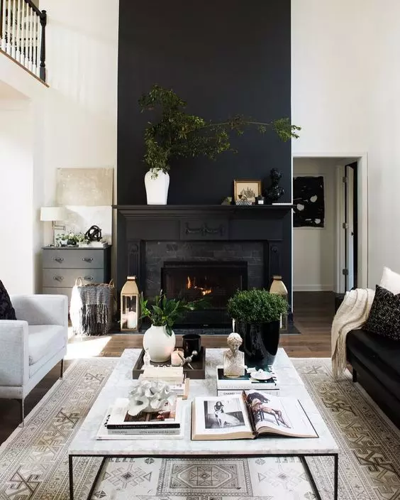 a cozy black and white living room with a built in fireplace, a black sofa and neutral chairs, a neutral coffee table, potted greenery and lanterns