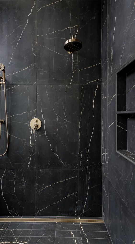 a dramatic black and gold shower space with large scale tiles, a niche for storage, gold fixtures is a lovely space