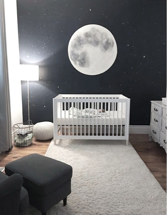 a dreamy black and white nursery with a celestial accent wall, a white crib with white bedding, a black chair with a footrest, a white dresser
