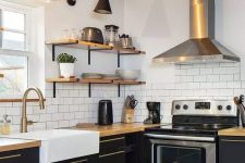 a farmhouse black and white kitchen with matte cabinets, butcherblock countertops, wooden shelves and a ceiling, a shiny metal hood