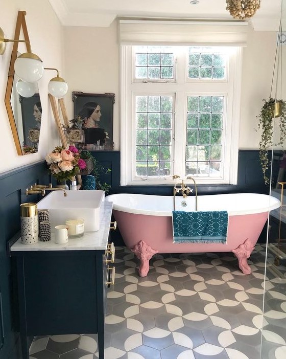 a gorgeous pink roll top clawfoot bathtub and statement tiles on the floor, all pulled together with a navy decor and statement lighting
