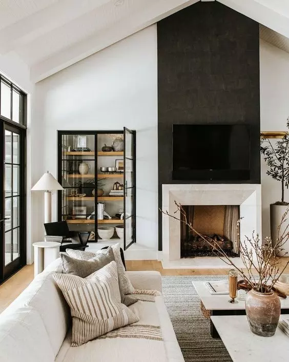 a jaw-dropping black and white living room with a large fireplace, a built-in display unit with black frame doors, white seating furniture and low coffee tables