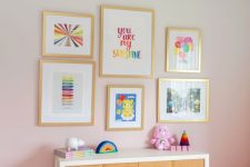 a kid’s space with an ombre pink accent wall, a stained dresser, a colorful gallery wall and bright toys plus a colorful chandelier