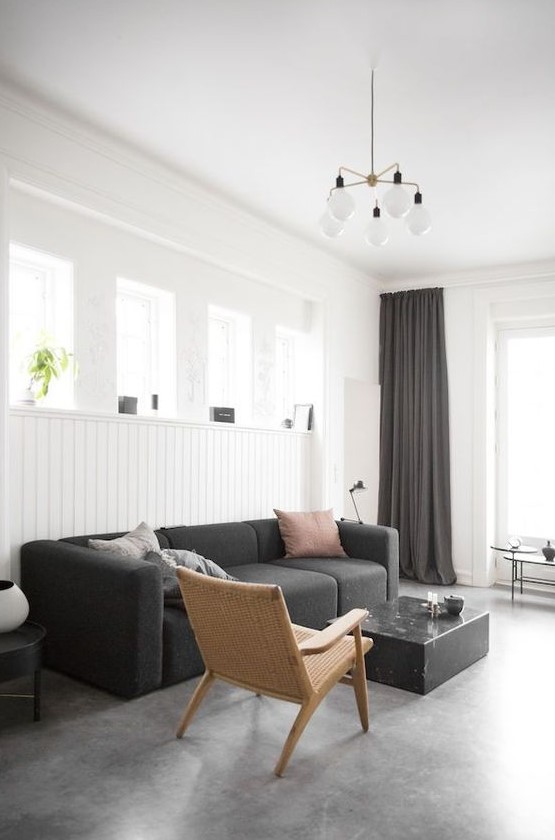 a laconic monochromatic living room with white beadboard walls, black furniture and textiles and a stone floor