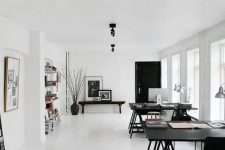 a large black and white Scandinavian home office with two large black desks and black chairs, a wooden bench, bookshelves and silver table lamps plus lots of natural light