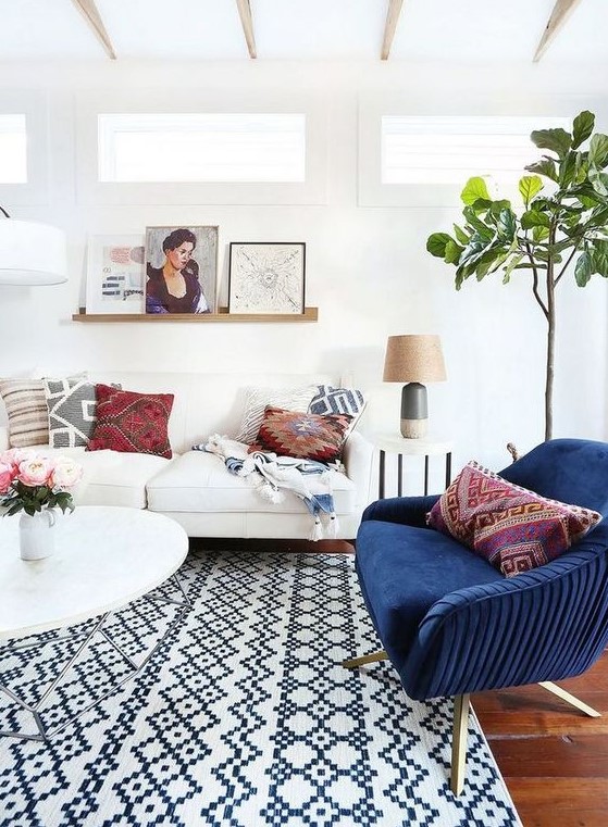 a light filled eclectic living room with several geometric prints, a navy chair, potted greenery and artworks