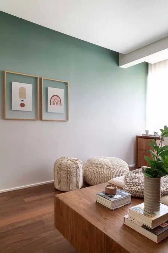 a lovely boho living room with an ombre green accent wall, a mini gallery wall, a stained dresser, a couple of neutral poufs and a stained table with books and plants