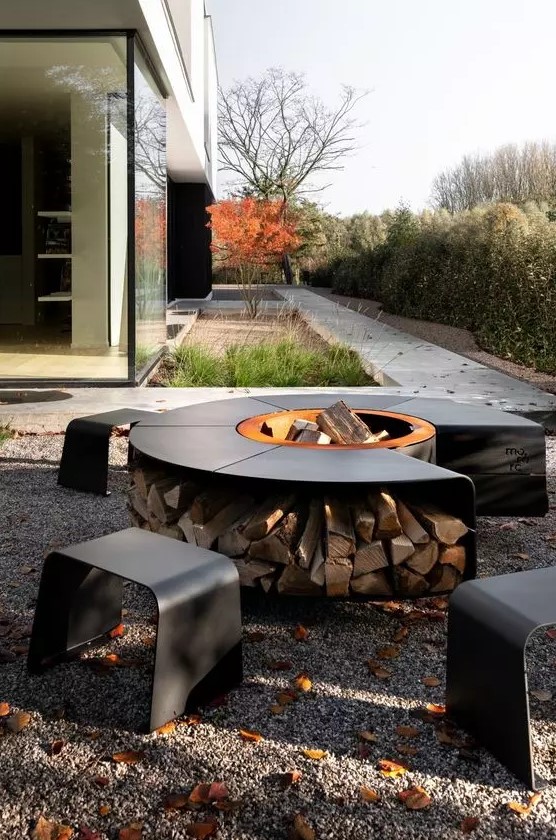 a lovely contemporary fire pit with a bowl in the center surrounded with a table and firewood storage plus matching blackened steel stools