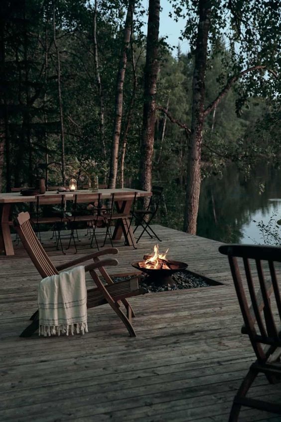 a lovely deck at the lake, with a rustic dining space with wooden furniture, a fire bowl, wooden chairs is a cool space