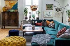 a lovely eclectic living room with a green sectional, a coffee table, a navy stool and a yellow ottoman, a stained credenza and artwork